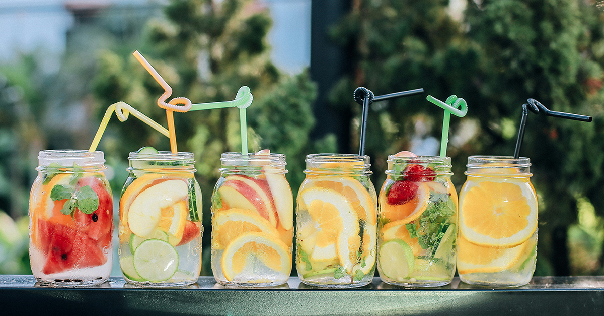 photo of six mason jars filled with a variety of fresh citrus fruits, watermelon and herbs, with colorful straws