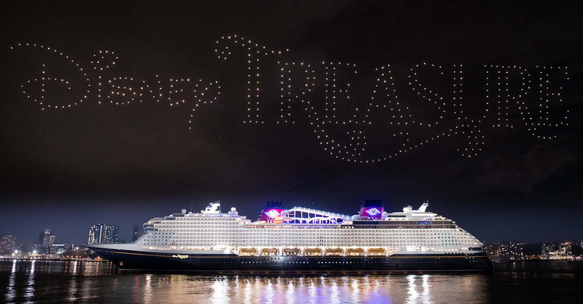 photo of the Disney Treasure, Disney's newest cruise ship, during its christening at night, with drones in formation above spelling out "Disney Treasure" 