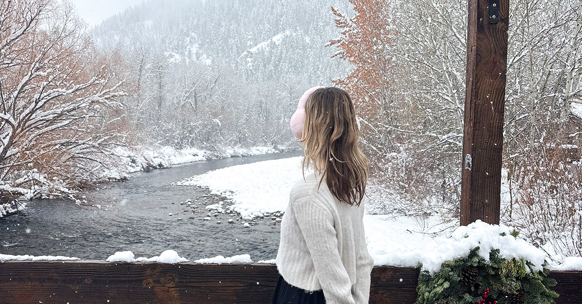 a young girl looks out at a snowy landscape with a river, wearing earmuffs